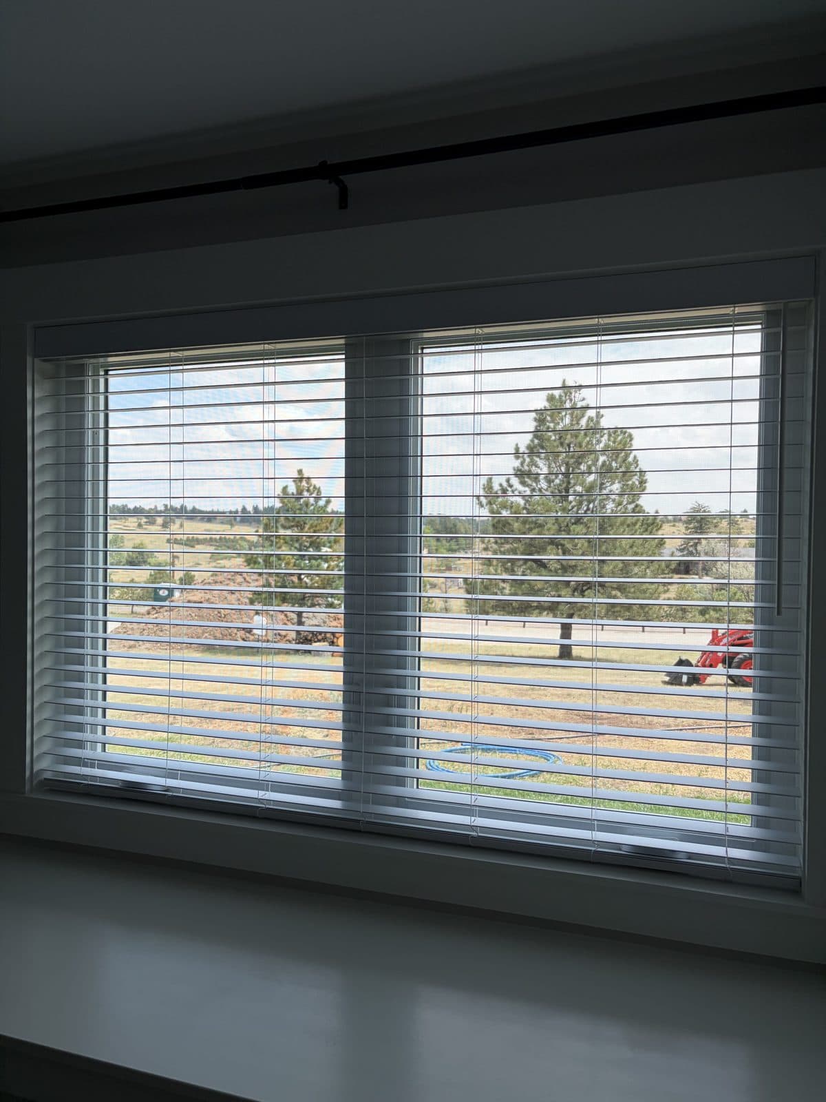 White blinds on a wide double window looking out over open pasture