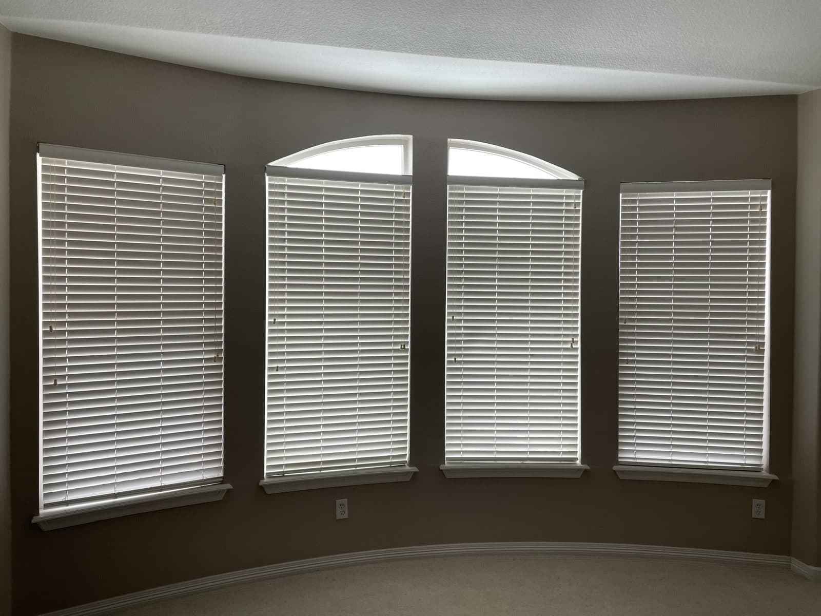 Four tall windows in a curved bay wall fitted with white blinds below two arched tops