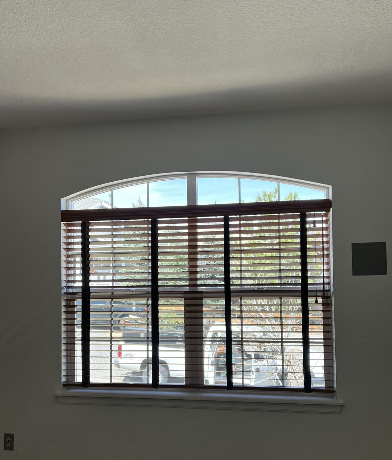 Wood-tone blinds with dark cloth tapes below an uncovered arched transom