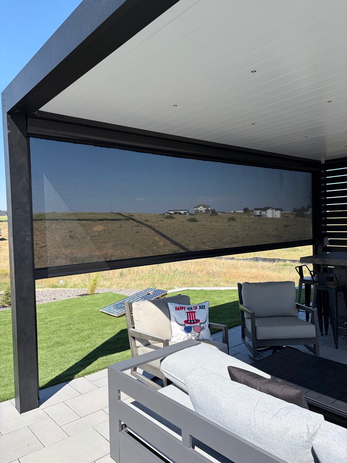 A wide exterior screen on a modern louvered pergola over a paver patio