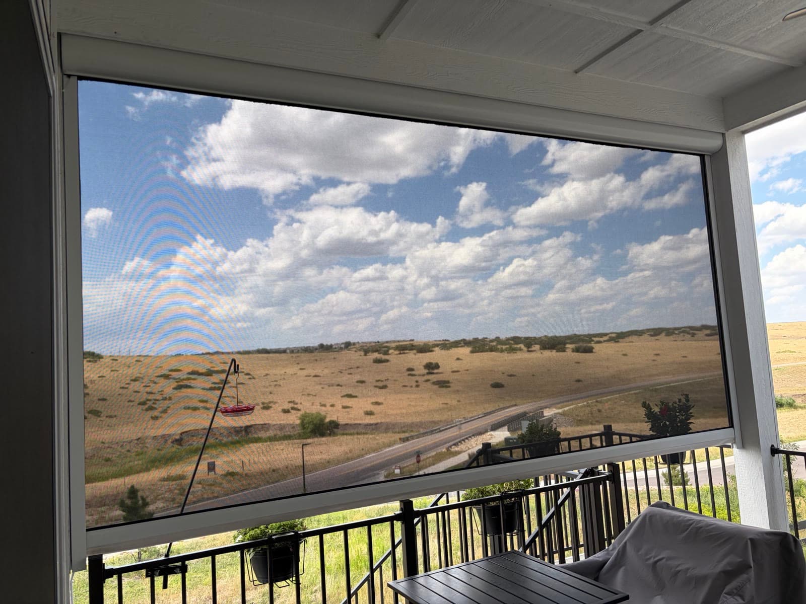 An exterior shade lowered over a covered deck with prairie and cloud views