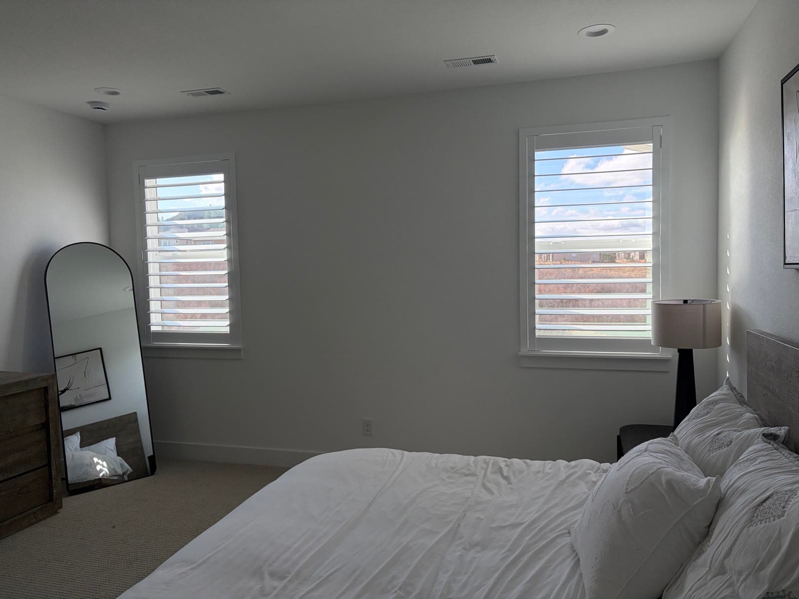 Plantation shutters on two bedroom windows beside a leaning floor mirror