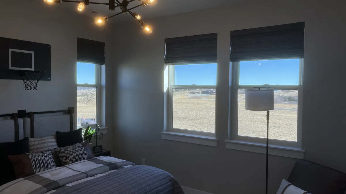 A bedroom with woven roman shades raised over three windows and a Colorado morning view.