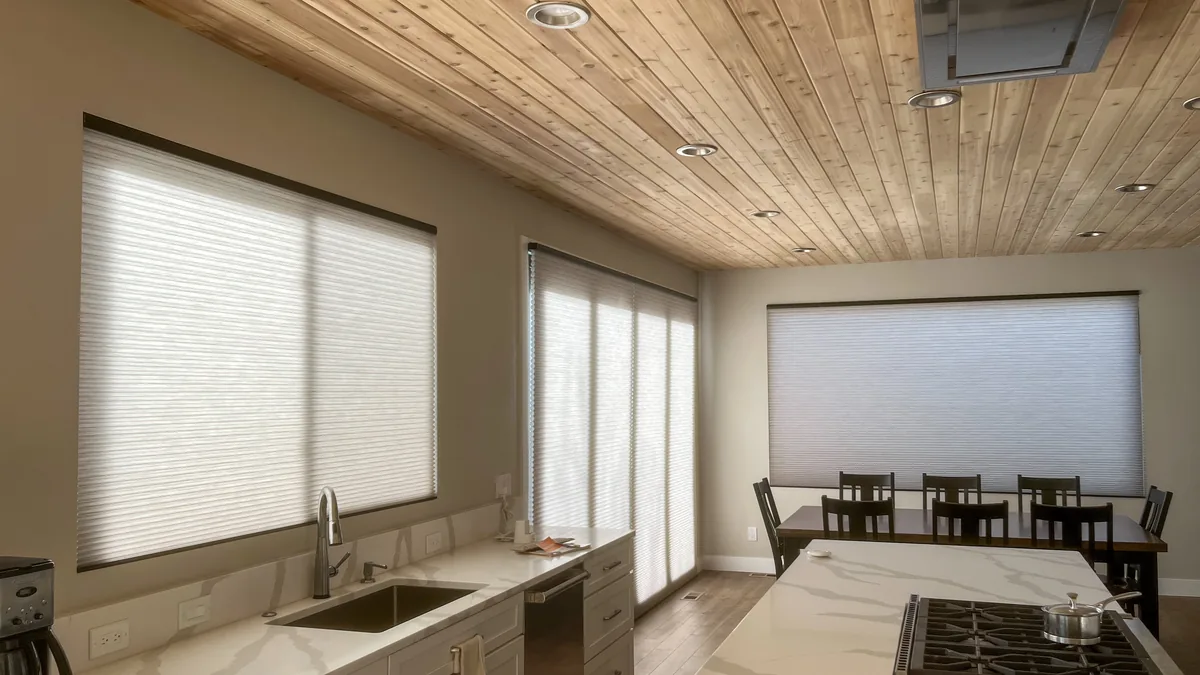 A bright kitchen with cellular shades on the windows above the counter and a wood-plank ceiling.